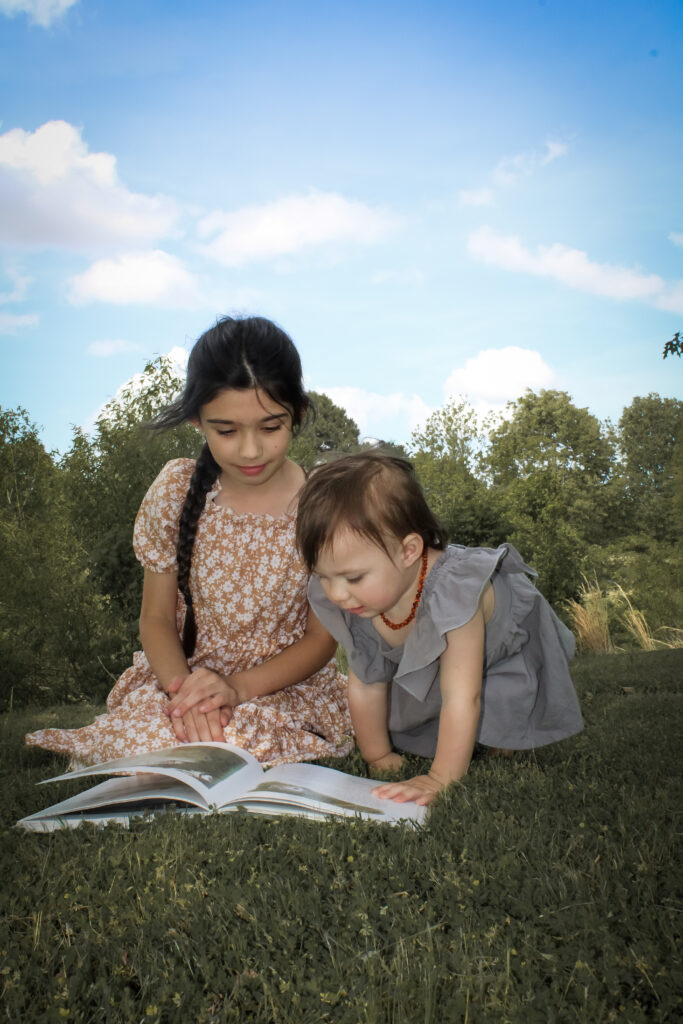 Two girls reading books about courage for kids together sitting on the grass.