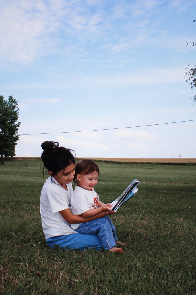 Girl and baby reading a book in the grass.